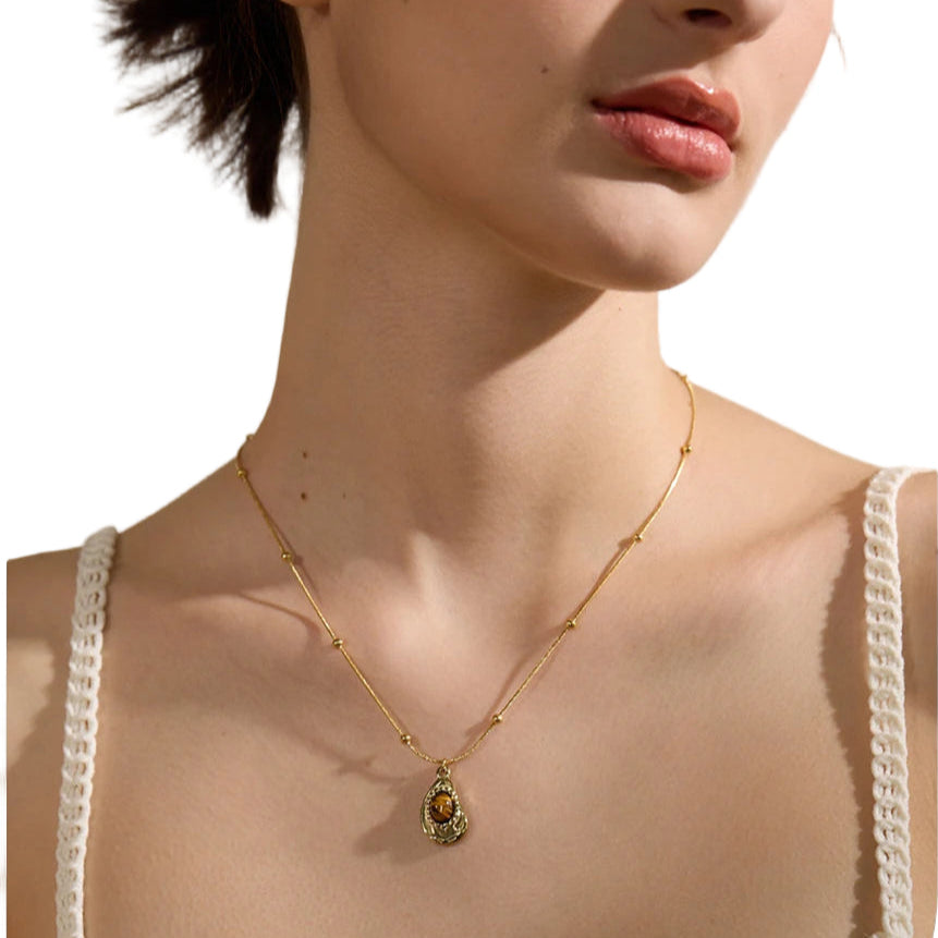 Woman wearing a gold necklace with a pendant against a neutral background