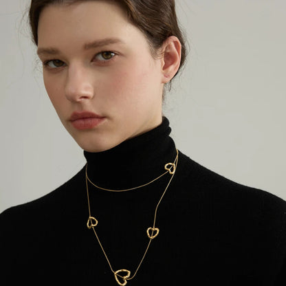 Woman wearing a gold necklace with heart pendants against a neutral background