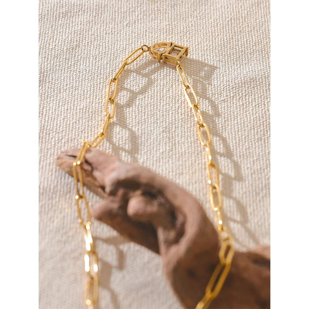 Gold chain necklace held by a hand against a textured beige background