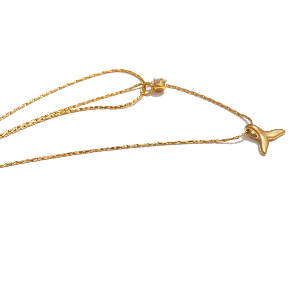 Gold necklace with a whale tail pendant on a white background
