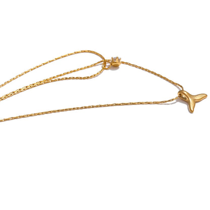 Gold necklace with a whale tail pendant on a white background