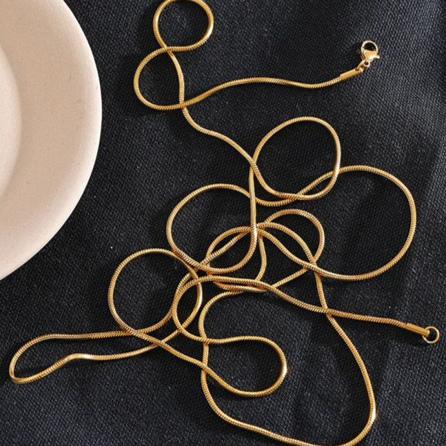 Gold necklace on a dark fabric background with a white bowl.
